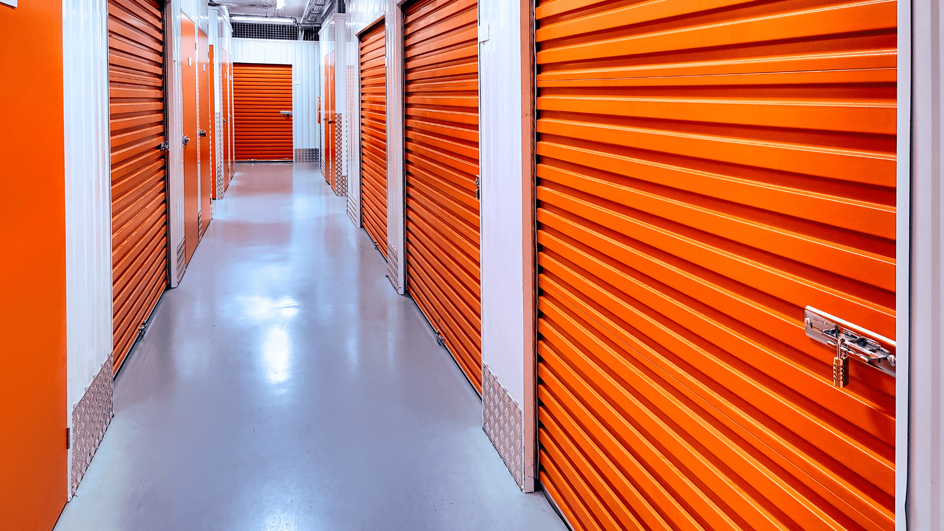 A long corridor of orange self-storage unit doors