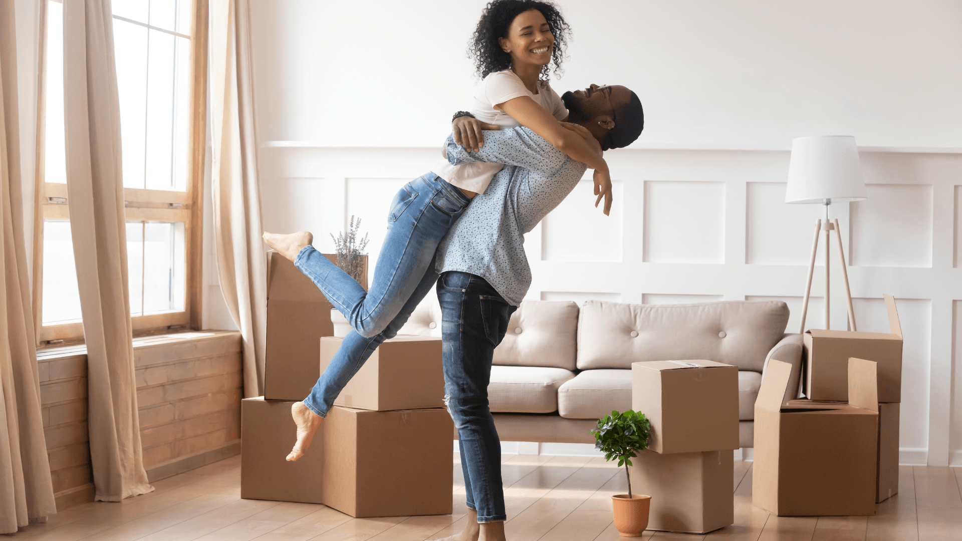 A couple embracing joyfully among moving boxes in a sunlit living room