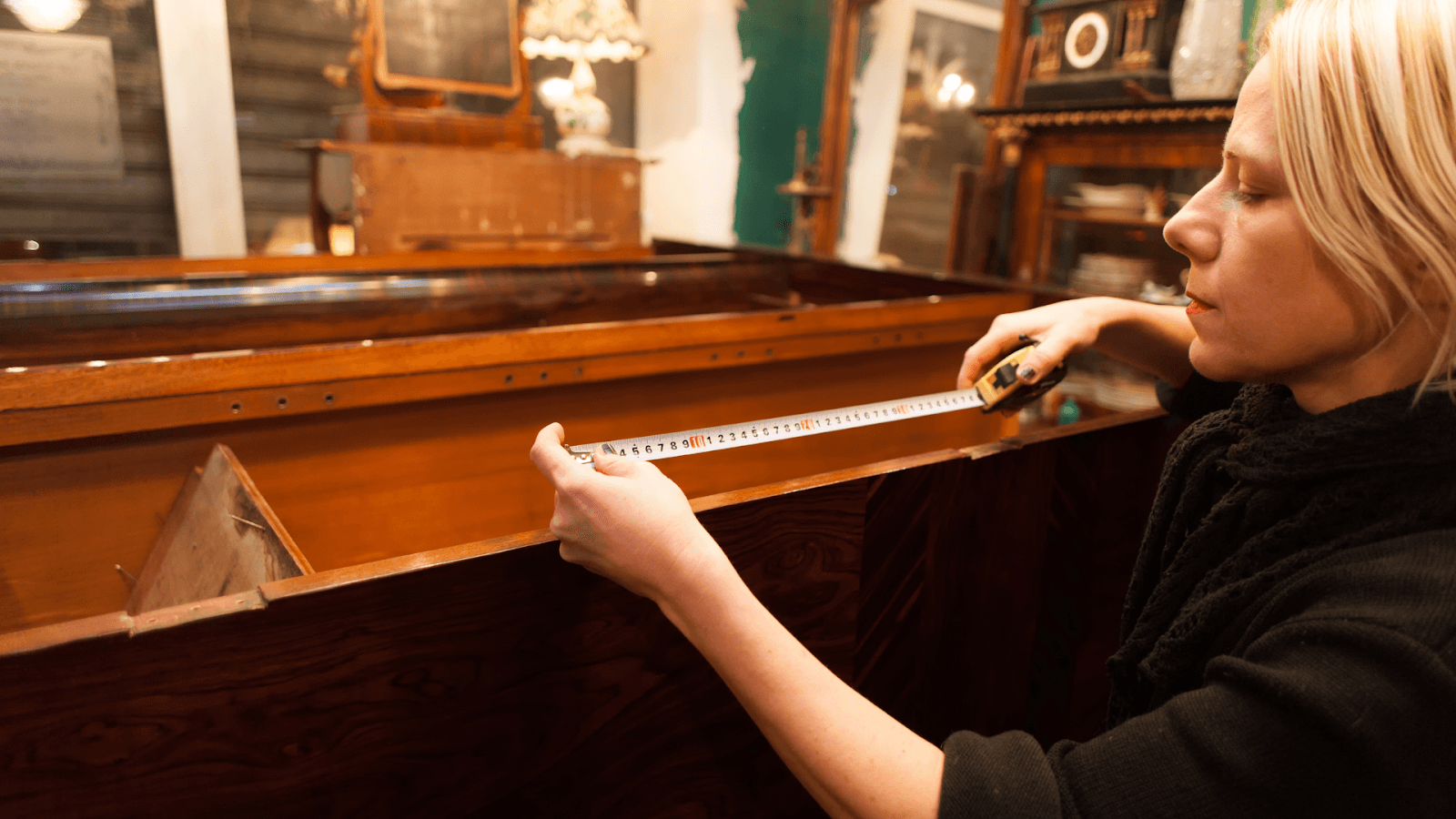 A woman measuring a large antique cabinet with a tape measure before a move