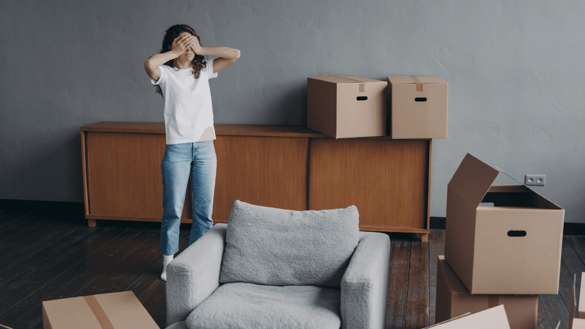 An overwhelmed person holding their head among moving boxes